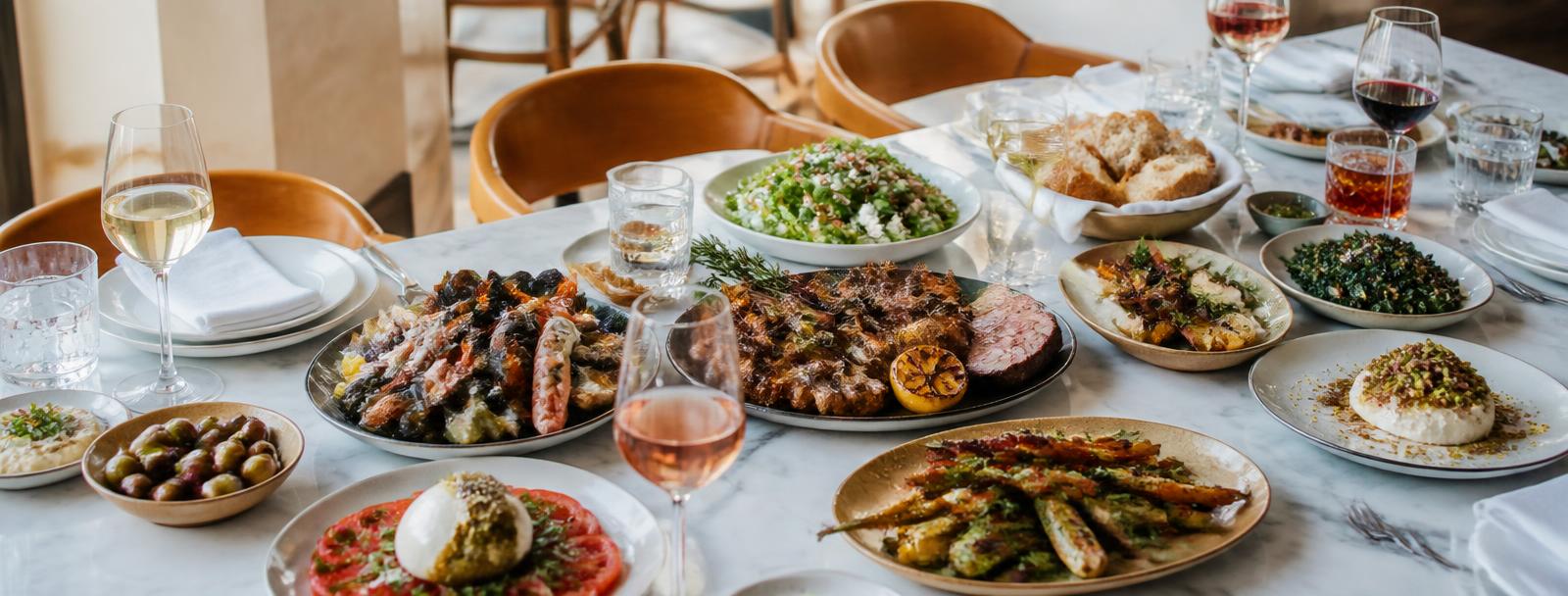 Gedeckte Tafel mit kleinen Tellern, Gegrilltem, Meeresfrüchten, Salaten, Dessert und Wein, Tageslicht
